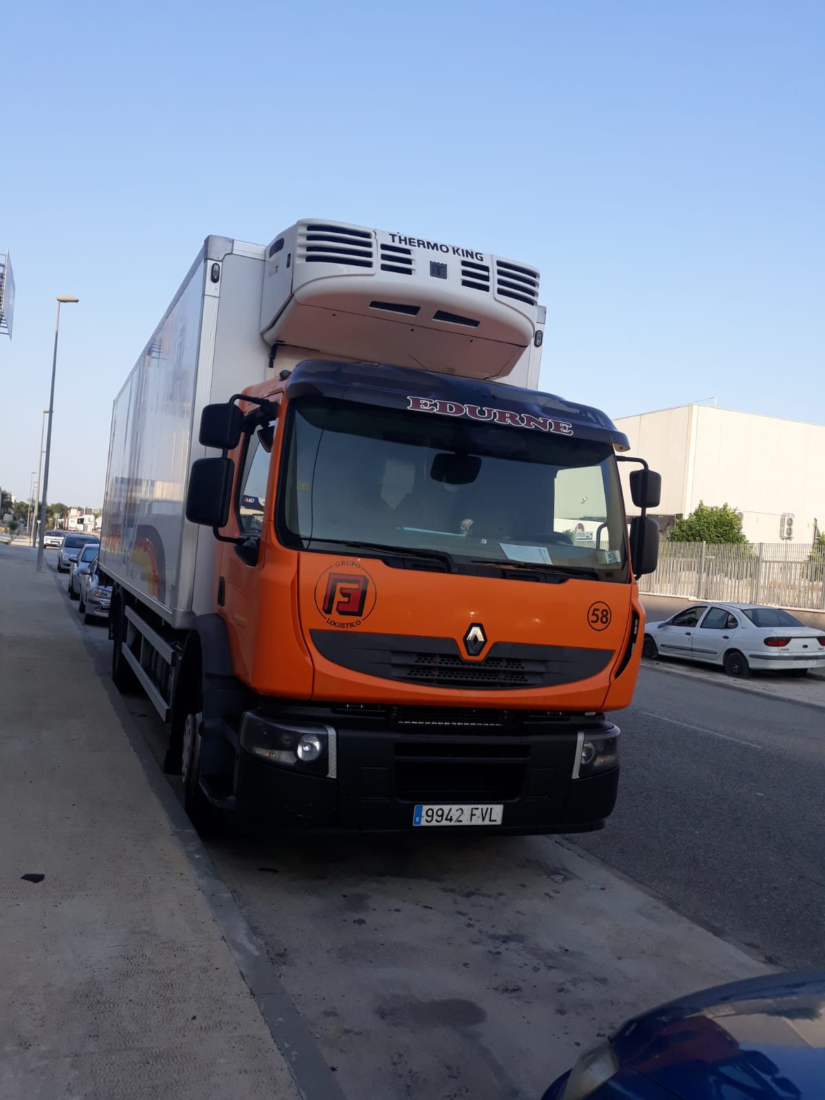 Camión naranja con la inscripción "EDURNE" y la marca "Grupo Fuentes Logístico" estacionado en la calle durante el día.