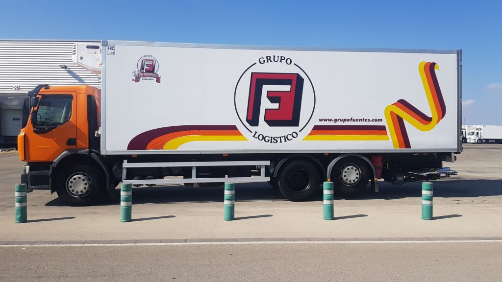 Camión de reparto naranja y blanco del Grupo Fuentes Logístico estacionado en un área de carga.