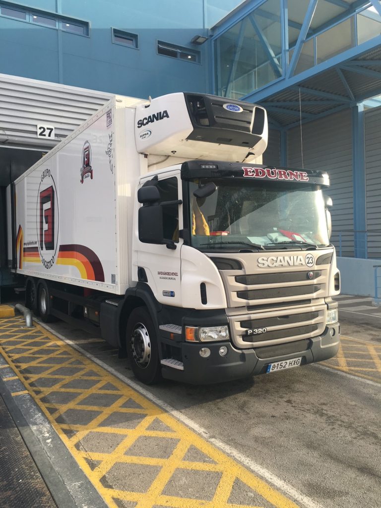 Camión Scania P320 blanco con la inscripción "EDURNE" estacionado en una bahía de carga.